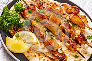 Grilled chicken kebabs sprinkled with chopped fresh parsley over flatbreads on plate on white wooden table
