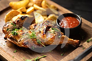 Grilled chicken leg with potatoes and tomato sauce on wooden board on table