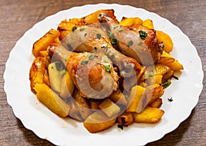 Grilled chicken leg and potatoes on the white plate on a wooden