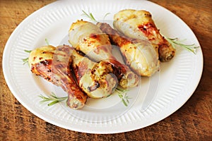 Grilled chicken legs with mustard on wooden table served on white plate with rosemary. BBQ dinner background