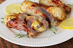 Grilled chicken legs with mustard on wooden table served on white plate with rosemary. BBQ dinner background