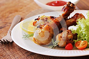 Grilled chicken legs with mustard on wooden table served on white plate with rosemary. BBQ dinner background