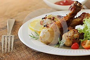 Grilled chicken legs with mustard on wooden table served on white plate with rosemary. BBQ dinner background