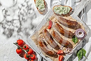 Grilled chicken meat sousage on white wooden plate with herbs and fresh vegetables. Sunny day, barbeque. Indgridients on a table,