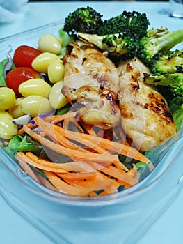 Grilled chicken placed on a salad in a clear bowl