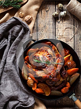 Grilled chicken with potatoes and vegetables in a cast-iron frying pan on a wooden rustic background. Close-up. View