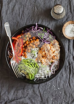 Grilled chicken, rice, spicy chickpeas, avocado mash, cabbage, pepper buddha bowl on dark background, top view.