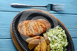 Grilled Chicken Steak with fried potatoes in rural style and coleslaw salad served in a tray over blue background.