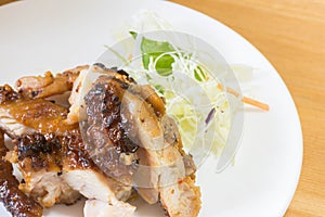 Chopped grilled chicken breast barbecue in a white plate saucer with green leafy vegetables on the side as garnish.