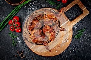 Grilled chicken wings on a dark stone table with vegetables, cream and tomato sauce. Served on a wooden board. Fast food restauran