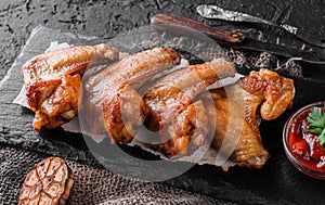 Grilled chicken wings meat with tomato sauce on slate board over dark background. Top view