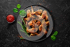 Grilled chicken wings with sauce and spices on a black stone plate.