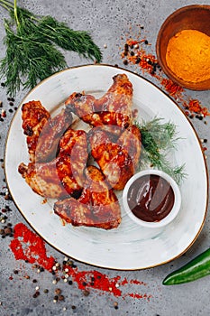 Grilled chicken wings with tomato sauce on white plate on grey background top view