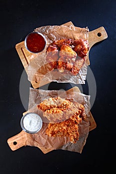 Grilled chicken wings on a wooden board. Two types of chicken wings with sauce. An appetizer for beer. Vertical photo.