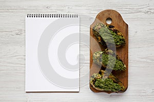 Grilled chimichurri chicken breast on a rustic wooden board, blank notepad on a white wooden background, top view. Copy space