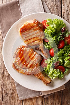 grilled chop pork honey glaze, served with a salad of fresh vegetables close-up on a plate. Vertical top view