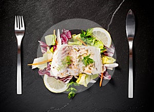 Grilled cod fillet with salad on black slate plate