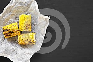 Grilled corn on the cob ove black background, top view. Summer food. From above, flat lay.