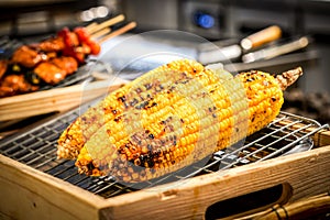 Grilled corn on the grill with blur BBQ beside.