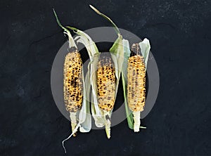 Grilled corn over black slate stone background, top view.