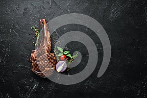 Grilled cowboy beef steak, herbs and spices on a black stone background. Barbecue. Top view.