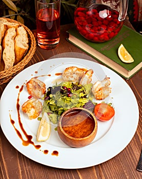 Grilled crevettes with green salad, tomatoes, lemon and dip sauce in white plate. photo