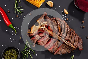 Grilled cut meat on rustic black background. Fried steak on bone, restaurant serving with spices and herbs, top view