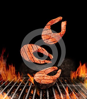 Grilled delicious salmon steaks are falling down on black background. Barbecue bbq grill, flaming fire, ember charcoal