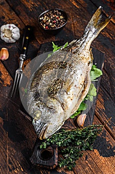 Grilled Dorada sea bream fish on a cutting board. Dark wooden background. Top view