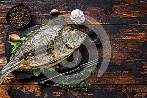 Grilled Dorada sea bream fish on a cutting board. Dark wooden background. Top view. Copy space