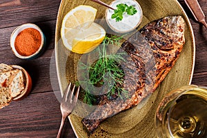 Grilled dorado fish with lemon and greens on plate on wooden background