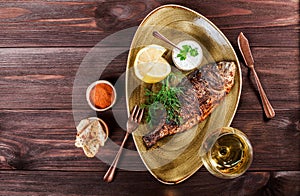 Grilled dorado fish with lemon and greens on plate on wooden background. Delicious dish of seafood.