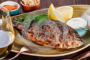Grilled dorado fish with lemon and greens on plate on wooden background. Delicious dish of seafood