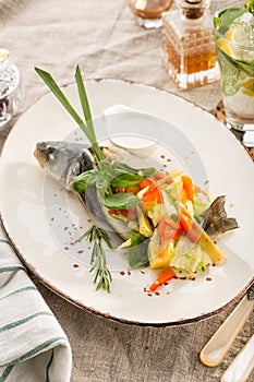 Grilled dorado fish stuffed with different vegetables on white plate served on the table