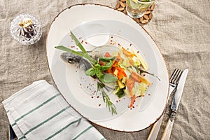 Grilled dorado fish stuffed with different vegetables on white plate served on the table