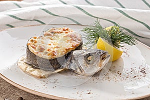 Grilled dorado fish stuffed with melted cheese on white plate with lemon on tablecloth