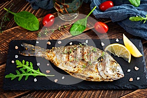 Grilled dorado fish on wooden background. Roasted seafish with spice and herbs