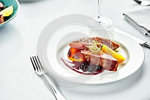 Grilled duck breast with peaches in berry sauce, grilled duck fillet on a white plate, banquet serving of duck meat on a