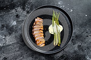 Grilled Duck fillet steaks with asparagus. Black background. Top view