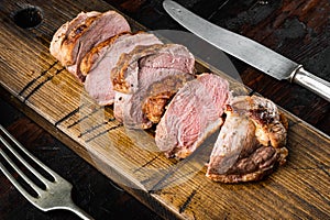 Grilled duck meat, on wooden serving board, on old dark  wooden table background