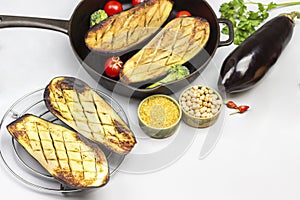Grilled eggplants on wire rack and in pan with vegetables and groats