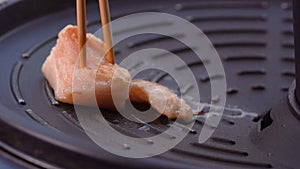 Grilled fatty pork meat in chopsticks on hot steam smoke water from hot pan for cooking in party