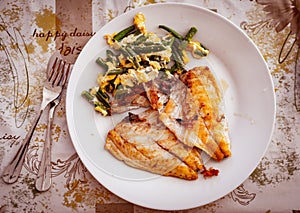 Grilled fish fillet and scrambled eggs and vegetables on plate, top view