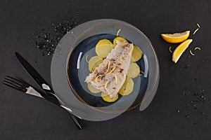 Grilled fish fillet served with potatoes on plate over black background