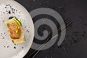 Grilled fish fillet served with zucchini on white plate over black background