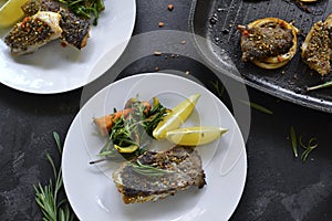 Grilled fish with lemon, herbs and rosemary. Fried fish fillets in a white plate. Beautiful presentation of food. Rucolla salad