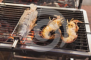 Grilled fish and lobsters lying on the charcoal grill over the red embers - street food in Bangkok
