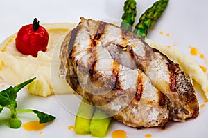 Grilled fish with mashed potatoes and asparagus on white plate