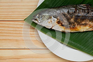 Grilled fish placed on banana leaf on a white plate