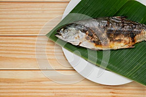 Grilled fish placed on banana leaf on a white plate